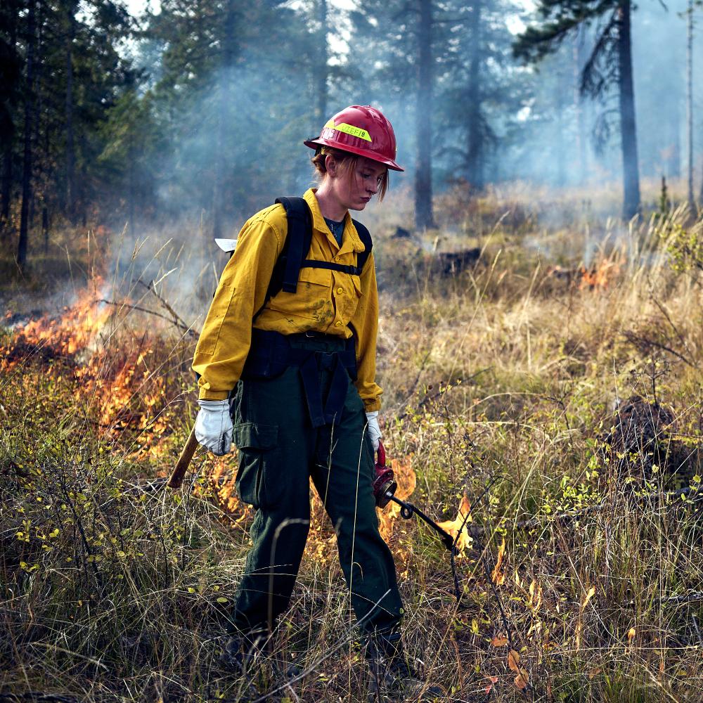 A worker in protective gear near a small fire.